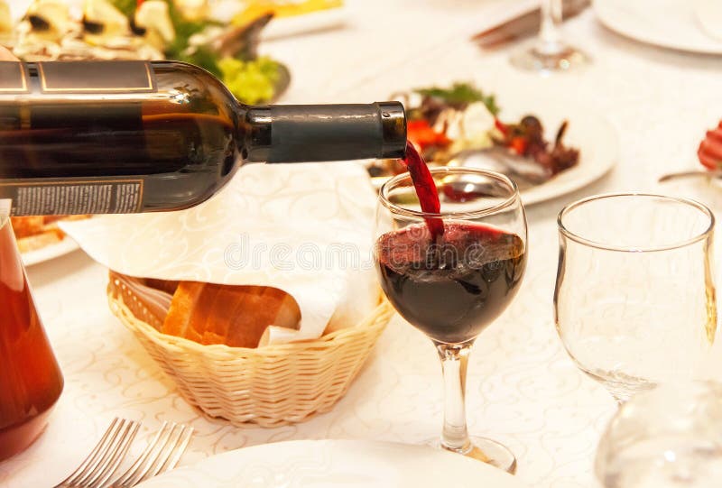 Red wine pouring into a wine glass, that standing on the table.