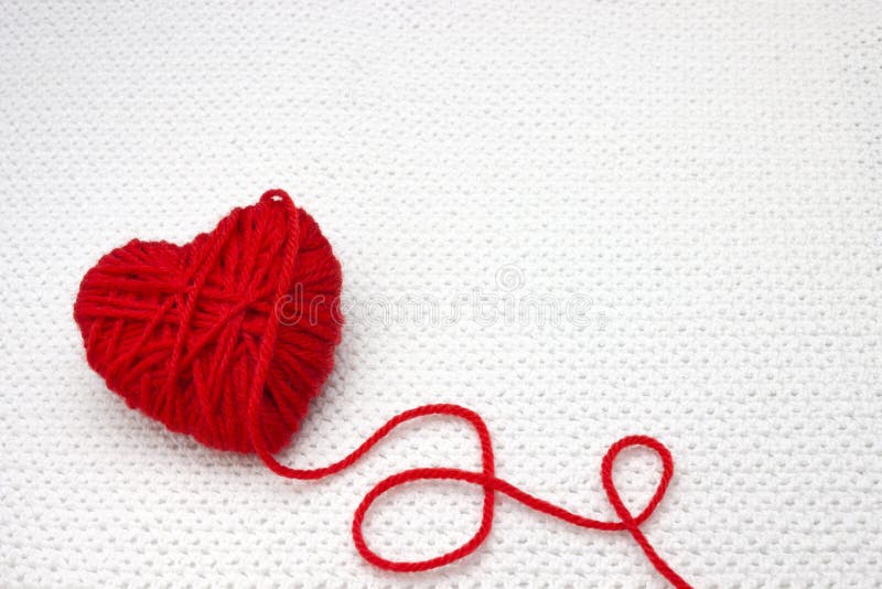 Red yarn ball like a heart on the white crochet background. Romantic Valentines Day concept. Red heart made of wool yarn with plac