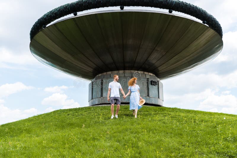 redhead couple holding hands and walking on grassy hill in front of modern stock photos redhead couple holding hands and walking on grassy hill in front of modern stock photos