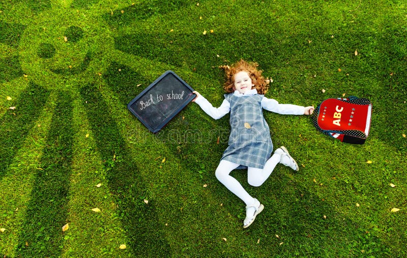 Redhead girl lying on the green grass in park, high top view.