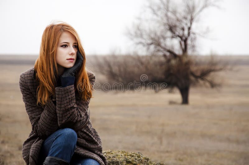 Redhead girl sitting at outdoor in autumn time.