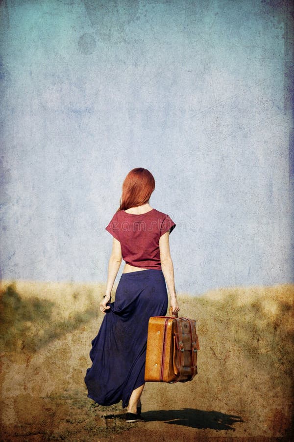 Redhead girl with suitcase at countryside road