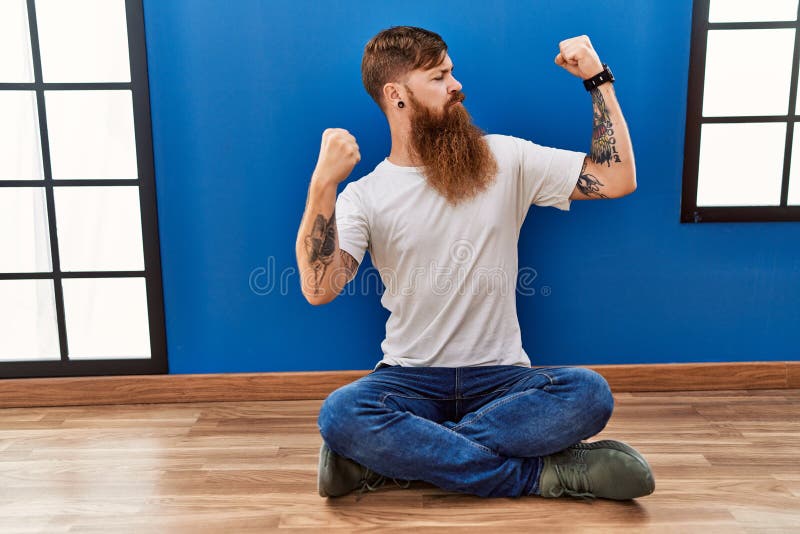 Redhead Man with Long Beard Sitting on the Floor at Empty Room Showing