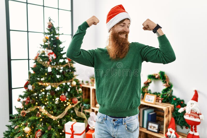 Redhead Man with Long Beard Wearing Christmas Hat by Christmas Tree