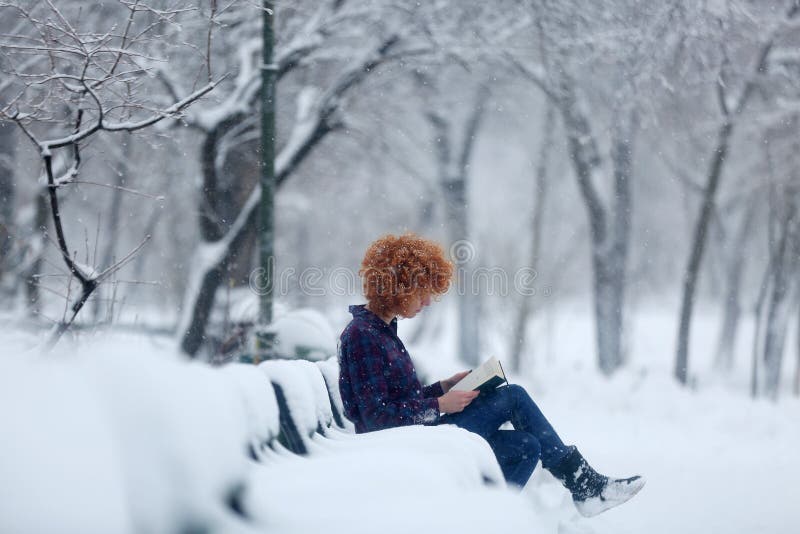 Donna seduta su una panchina piena di neve la lettura di un libro.