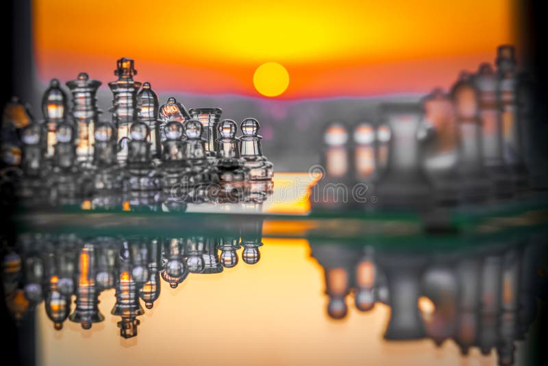 Reflected glass chess pieces with a sunset in the background stock photos
