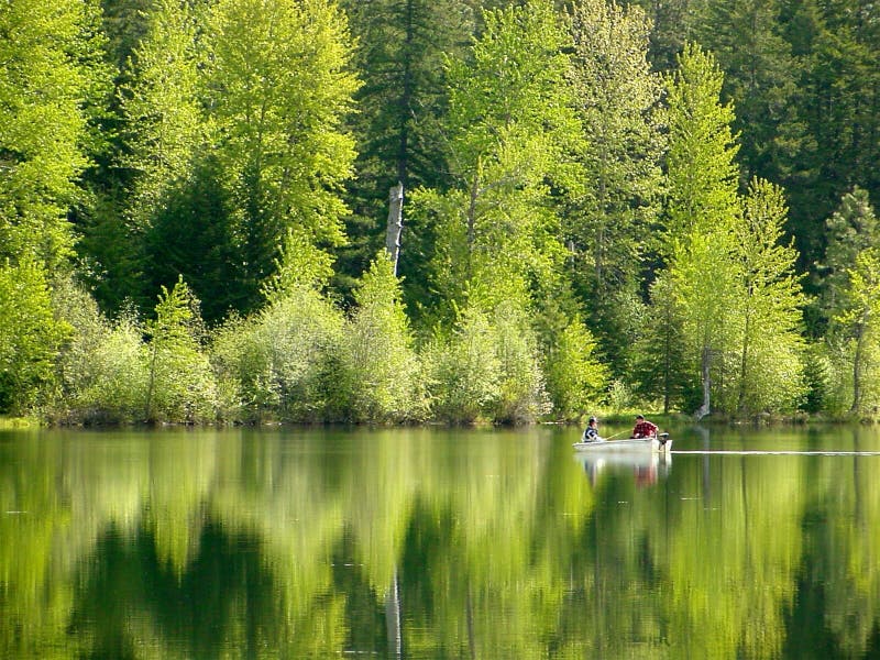 Due persone che pesca un giorno di primavera di un calmo lago verde.