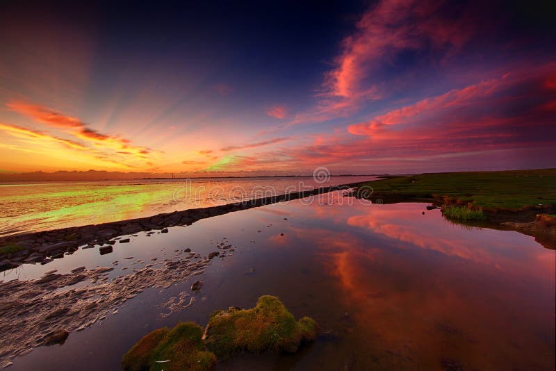 Reflection of the fiery sky in a puddle of sea during ebb on the Dollard in Groningen, the Netherlands. Reflection of the fiery sky in a puddle of sea during ebb on the Dollard in Groningen, the Netherlands