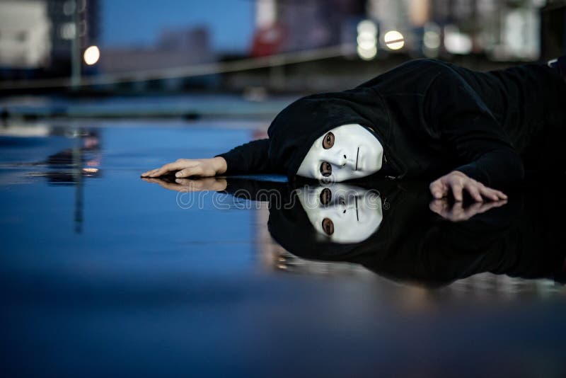 Reflection of mystery hoodie man in white mask feeling depressed and disappointed lying on wet floor after the rain. Sadness, royalty free stock image Reflection of mystery hoodie man in white mask feeling depressed and disappointed lying on wet floor after the rain. Sadness, royalty free stock image