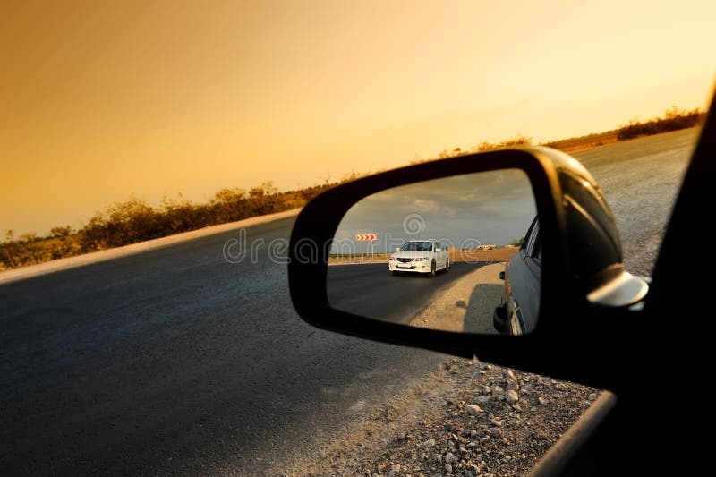 Reflection in the side car rear view mirror of a white car traveling along the road at sunset