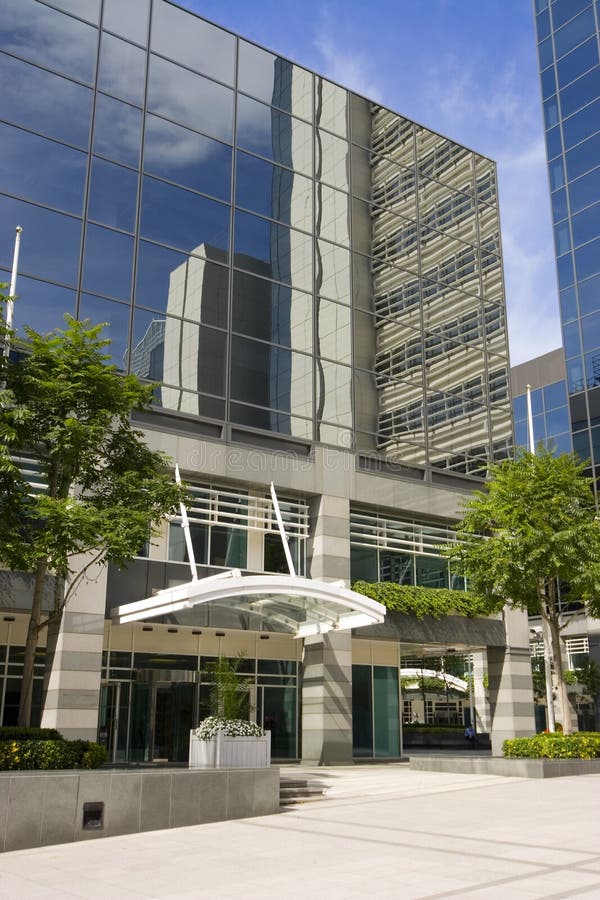 The entrance to a glass fronted office building with the reflections of surrounding buildings in the windows.