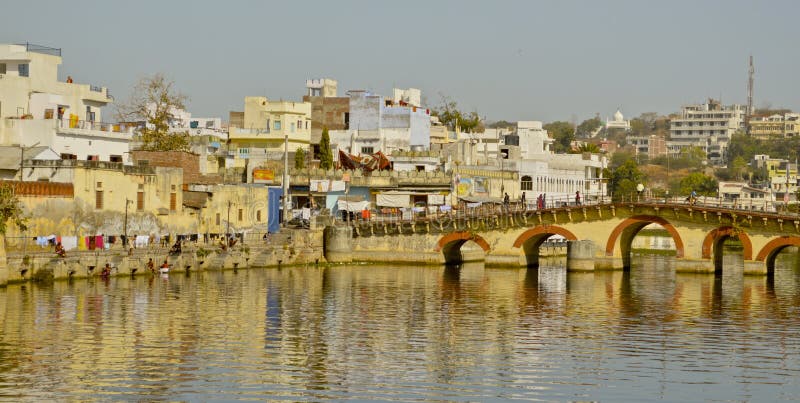 Reflections of bridge and buildings on the lake in Udaipur, a city in the Rajasthan region of Northern India. Known as the Venice of the East. Also shows people bathing and washing clothes at the side. Reflections of bridge and buildings on the lake in Udaipur, a city in the Rajasthan region of Northern India. Known as the Venice of the East. Also shows people bathing and washing clothes at the side.