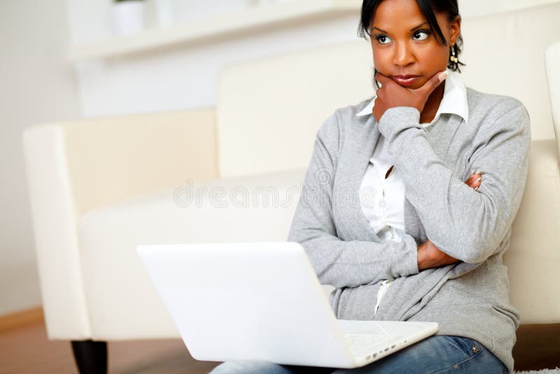 Portrait of a reflective young woman sits on the floor in front of her laptop at home indoor