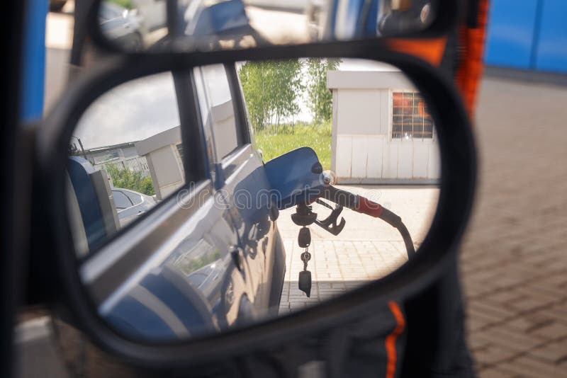 Reflejado en el espejo lateral de un coche del surtidor de gasolina para rellenar el combustible en coche en la gasolinera fotografía de archivo Reflejado en el espejo lateral de un coche del surtidor de gasolina para rellenar el combustible en coche en la gasolinera fotografía de archivo