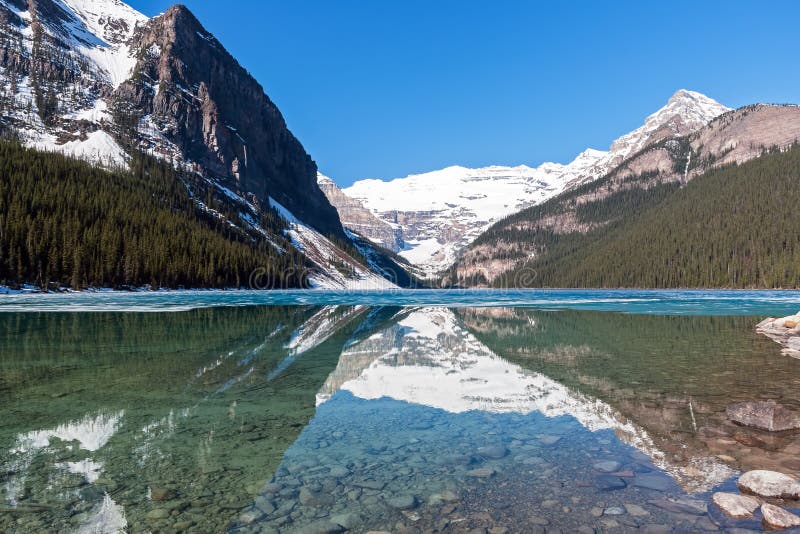 Snowy mountain reflection on half frozen lake Louise - Banff , Alberta, Canada. Shot was taken in late spring. Snowy mountain reflection on half frozen lake Louise - Banff , Alberta, Canada. Shot was taken in late spring.