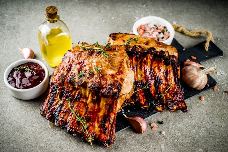 Grilled meat concept. bbq pork ribs with barbeque sauce, olive oil. fresh herbs on grey stone background copy space. Grilled meat concept. bbq pork ribs with barbeque sauce, olive oil. fresh herbs on grey stone background copy space