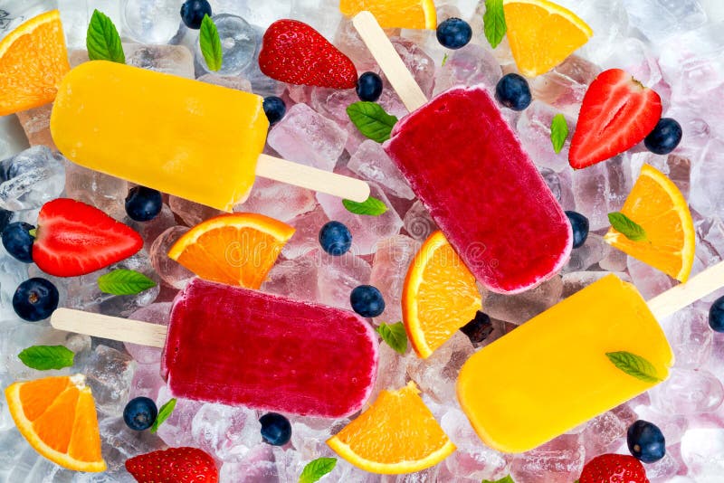 Refreshing fruit popsicle lollies on ice background with berries and peppermint.