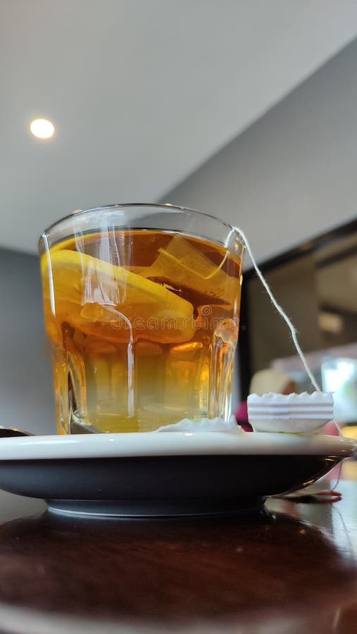 A refreshing lemon tea in a clear glass, with a tea bag tag, is on a saucer, conveying a serene moment. stock photography
