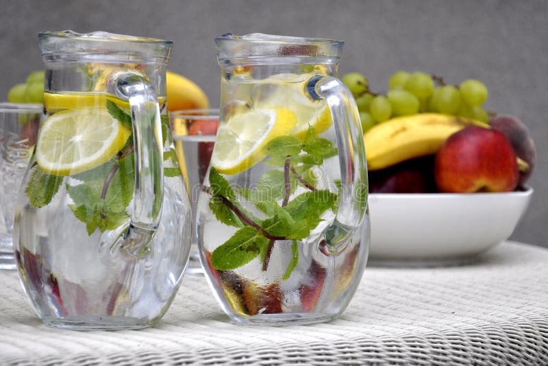 Caraffe di vetro con acqua fresca con la menta e il limone e ciotole piene di frutta tropicali qualche festa in giardino.