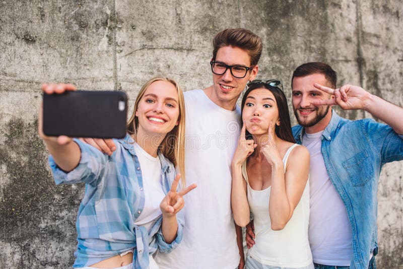 Refroidissez la photo de la société se tenant ensemble sur le fond gris La fille blonde prend le selfie de sa société Elle est photographie stock libre de droits Refroidissez la photo de la société se tenant ensemble sur le fond gris La fille blonde prend le selfie de sa société Elle est photographie stock libre de droits