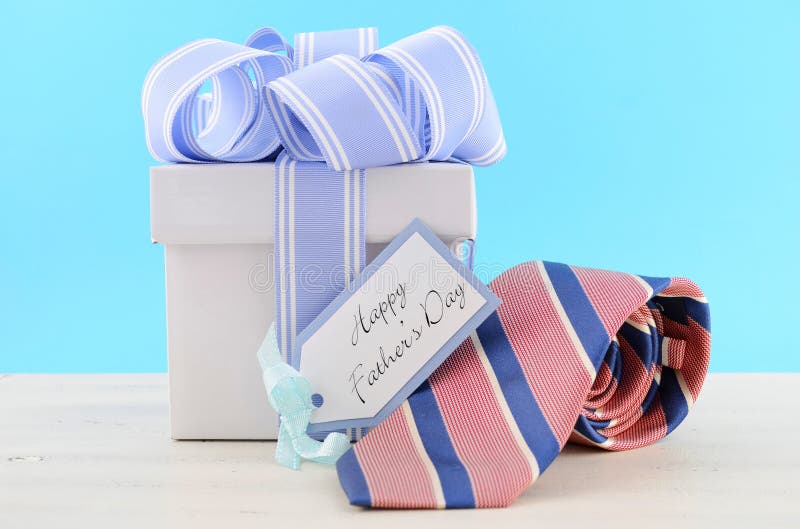Happy Fathers Day Gift with Blue and White Ribbon with red and blue stripe neck tie and gift tag on white wood table and pale aqua blue background. Happy Fathers Day Gift with Blue and White Ribbon with red and blue stripe neck tie and gift tag on white wood table and pale aqua blue background.