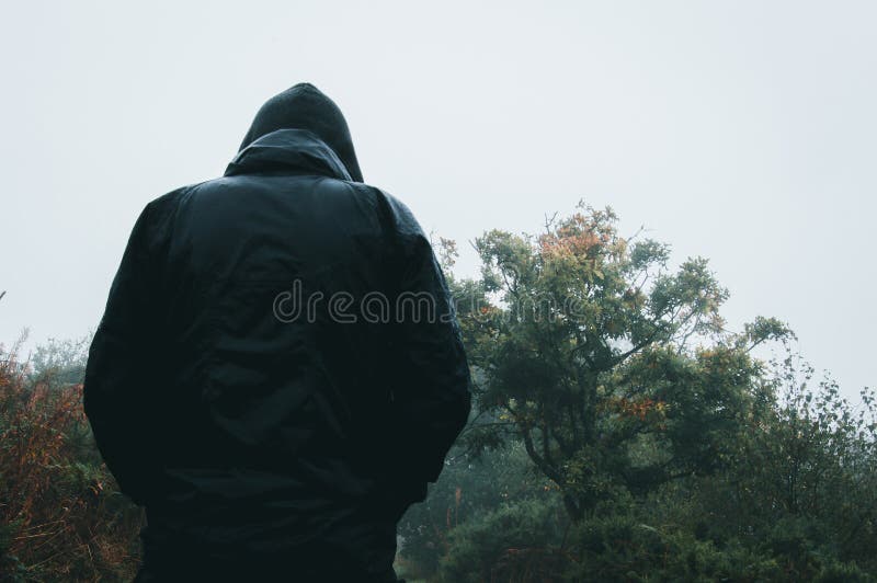Looking up from behind at a mysterious hooded figure wet from rain on a country path. Looking up from behind at a mysterious hooded figure wet from rain on a country path.