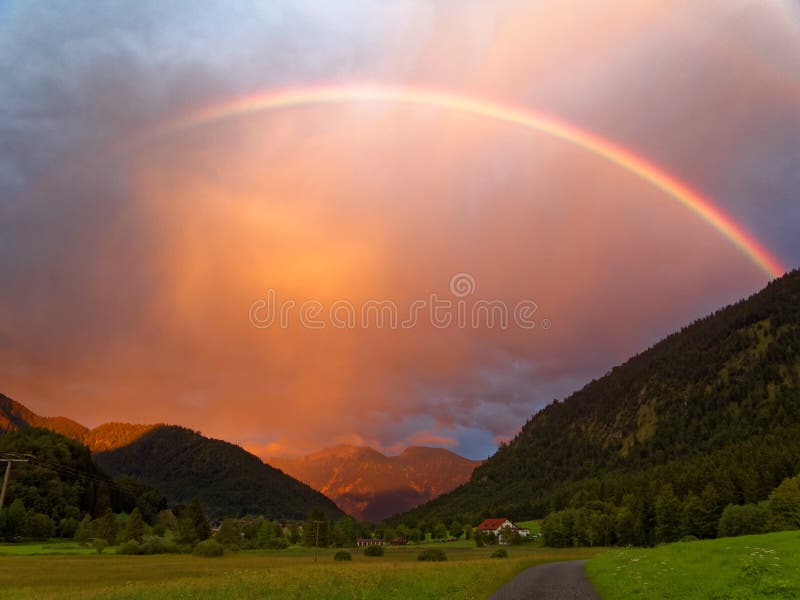 Regenboog door sinaasappel betrokken hemel in alpien landschap stock afbeelding Regenboog door sinaasappel betrokken hemel in alpien landschap stock afbeelding
