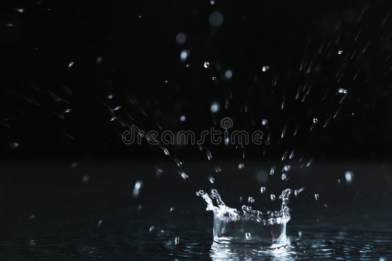 Rain drop falling down into puddle on dark background. Rain drop falling down into puddle on dark background