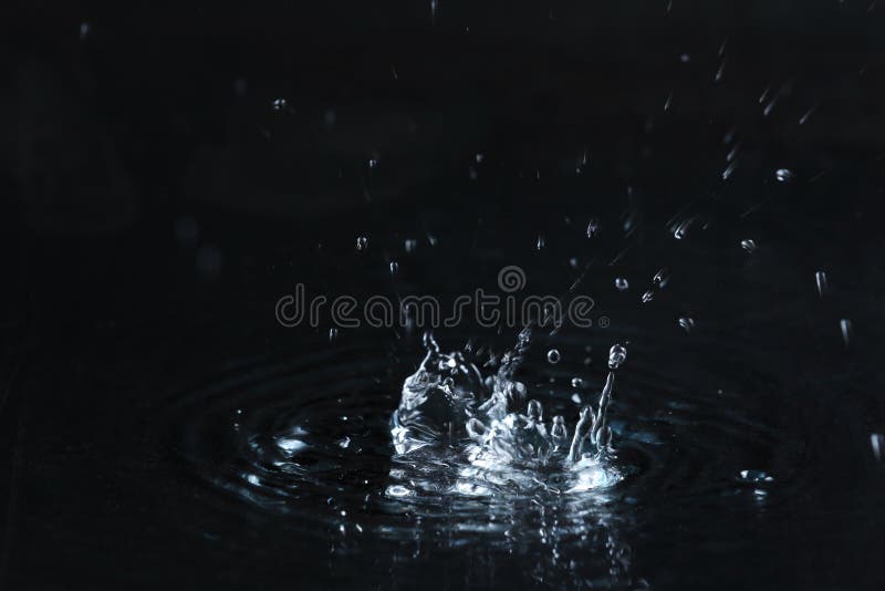 Rain drop falling down into puddle on dark background. Rain drop falling down into puddle on dark background