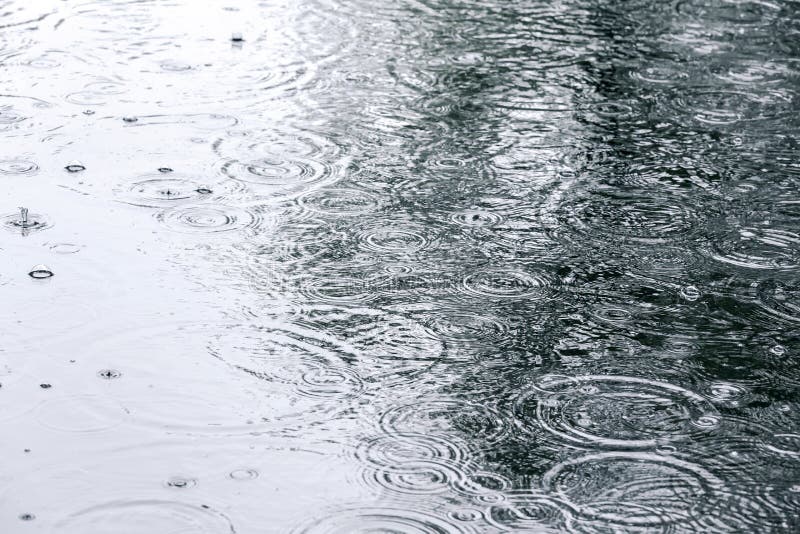 Raindrops and sky reflection on water surface of puddle on pavement. Raindrops and sky reflection on water surface of puddle on pavement