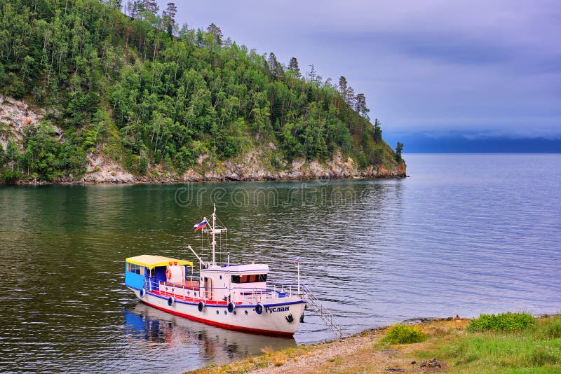 REGIÓN del LAGO BAIKAL, IRKUTSK, RUSIA - julio, 28 2016: Paisaje de Baikal con un yate que camina en orilla de la pequeña bahía fotografía de archivo REGIÓN del LAGO BAIKAL, IRKUTSK, RUSIA - julio, 28 2016: Paisaje de Baikal con un yate que camina en orilla de la pequeña bahía fotografía de archivo