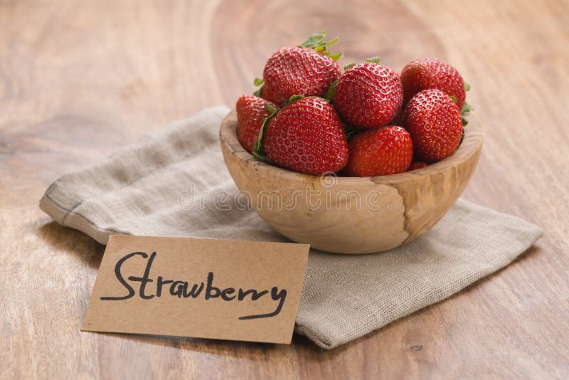 Reife Erdbeeren in der hölzernen Schüssel auf hölzernem Hintergrund mit Papierkarte lizenzfreies stockbild Reife Erdbeeren in der hölzernen Schüssel auf hölzernem Hintergrund mit Papierkarte lizenzfreies stockbild