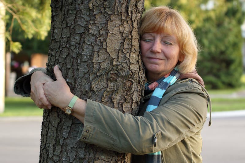A mature/senior woman hugging a tree outside in the suburbs. Health/peace/nature concept. A mature/senior woman hugging a tree outside in the suburbs. Health/peace/nature concept.