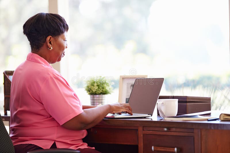 Reife Frau, die zu Hause Laptop auf Schreibtisch verwendet lizenzfreie stockfotografie Reife Frau, die zu Hause Laptop auf Schreibtisch verwendet lizenzfreie stockfotografie