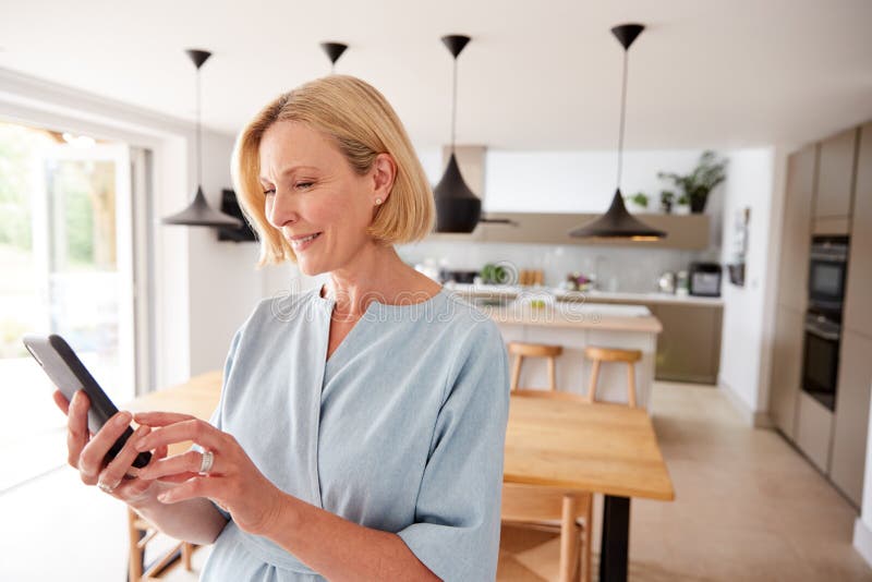 Reife Frauen nutzen App auf dem Mobiltelefon, um die Temperatur der Zentralheizung im Haus zu kontrollieren lizenzfreies stockfoto