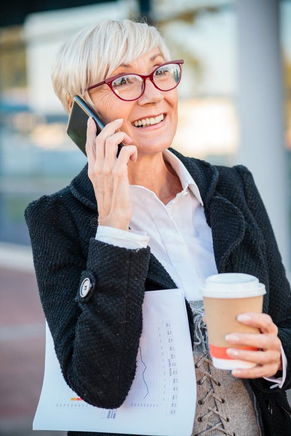 Reife Geschäftsfrau, die eine Pause vor einem Bürogebäude macht, telefonieren und Kaffee trinken lizenzfreie stockbilder Reife Geschäftsfrau, die eine Pause vor einem Bürogebäude macht, telefonieren und Kaffee trinken lizenzfreie stockbilder