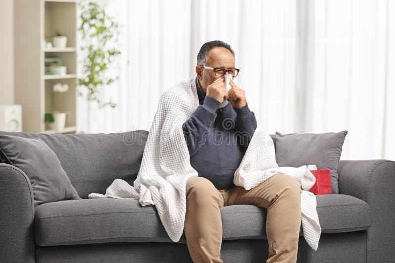 Reifender Mann fühlt sich unwohl und bläst Nase auf einem Sofa stockbilder
