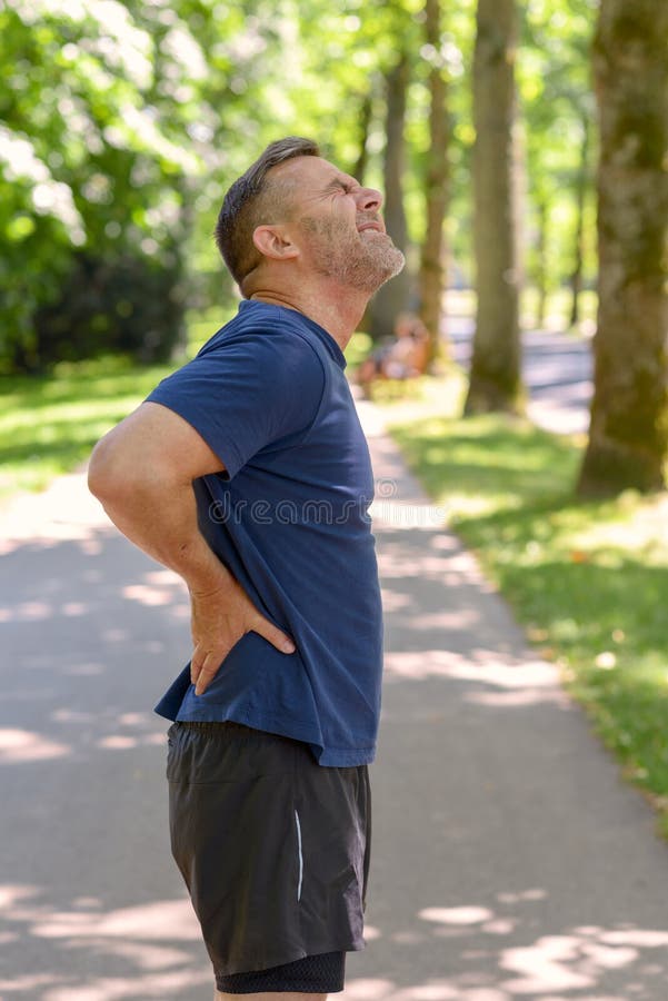Reifer Mann, der seine schmerzliche Rückseite nachdem dem Laufen hält lizenzfreie stockfotografie Reifer Mann, der seine schmerzliche Rückseite nachdem dem Laufen hält lizenzfreie stockfotografie