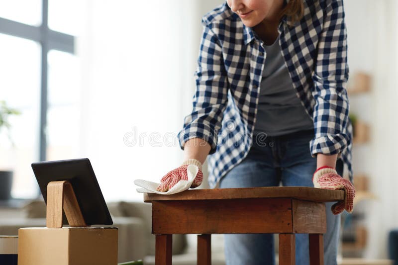furniture renovation, diy and home improvement concept - close up of woman with tablet pc computer cleaning or degreasing old round wooden table surface with paper tissue. furniture renovation, diy and home improvement concept - close up of woman with tablet pc computer cleaning or degreasing old round wooden table surface with paper tissue