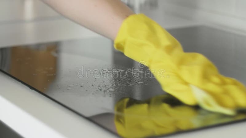 Reinigungs-cooktop, das Panel in der Küche mit fettem Entfernerspray und gelben Tuch durch eine Frau in den gelben Gummihandschuhe