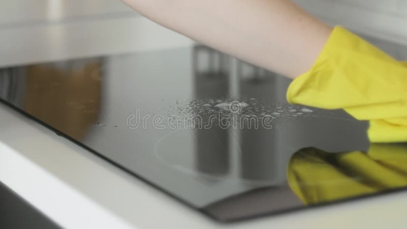 Reinigungs-cooktop, das Panel in der Küche mit fettem Entfernerspray und gelben Tuch durch eine Frau in den gelben Gummihandschuhe