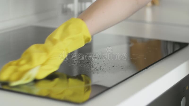 Reinigungs-cooktop, das Panel in der Küche mit fettem Entfernerspray und gelben Tuch durch eine Frau in den gelben Gummihandschuhe