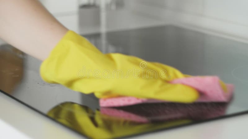 Reinigungs-cooktop, das Panel in der Küche mit fettem Entfernerspray und rosa Stofffetzen durch eine Frau in den gelben Gummihands