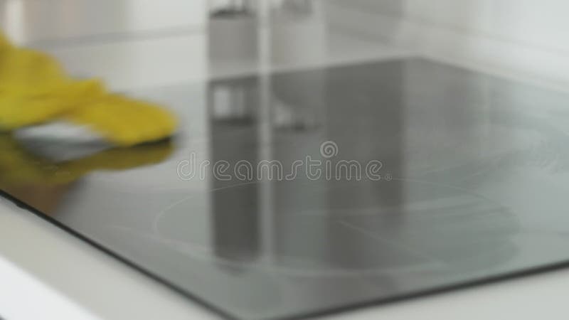 Reinigungs-cooktop, das Panel in der Küche mit fettem Entfernerspray und weißen Stofffetzen durch eine Frau in den gelben Gummihan