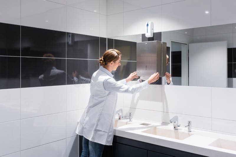 Reinigungsfrau, die öffentlich Toilette der Papierhandtücher wieder füllt lizenzfreies stockfoto Reinigungsfrau, die öffentlich Toilette der Papierhandtücher wieder füllt lizenzfreies stockfoto