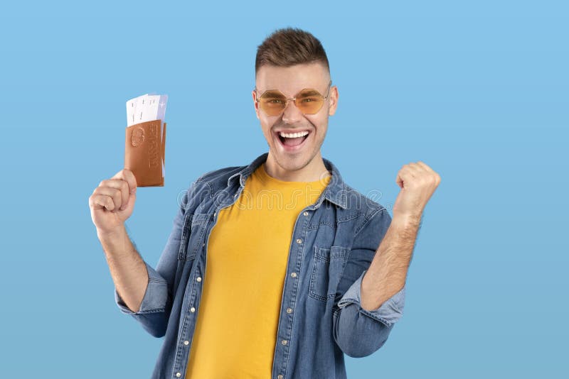 Reisekonzept. aufgeregt junge Kerl mit Pass mit Tickets und Geste ja über blaue Studio Hintergrund. tausendjähriger männlicher Tourist mit Dokumenten auf Überseereise