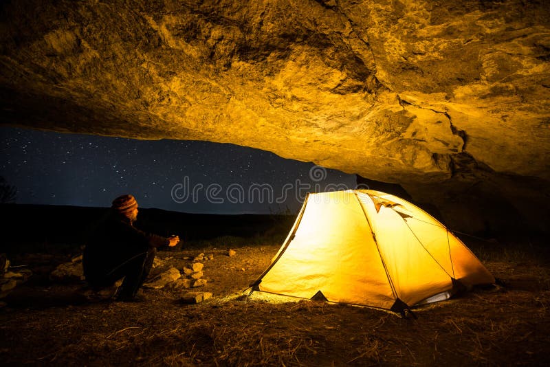 Reisender nahe dem glühenden Campingzelt in der Nachtgrotte unter einem sternenklaren Himmel lizenzfreies stockfoto Reisender nahe dem glühenden Campingzelt in der Nachtgrotte unter einem sternenklaren Himmel lizenzfreies stockfoto