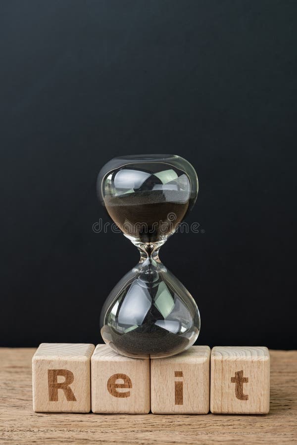 REIT, Real estate investment trust booming time concept, sandglass or hourglass on wooden cube block with alphabet building the stock photo