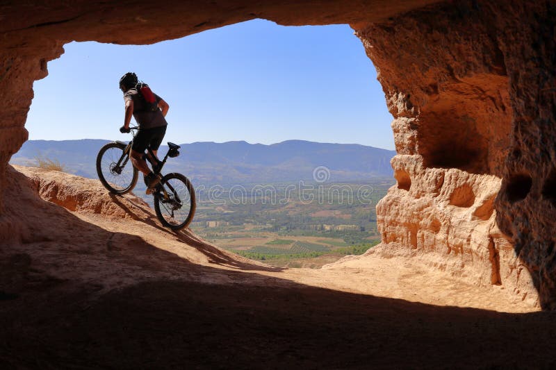 REITER MIT STURZHELM UND RUCKSACK IM SOMMER, DER EINE HÖHLE IN DER MOUNTAINBIKE MIT GROSSER ANSTRENGUNG LÄSST stockbilder