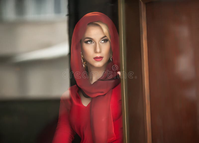 Reizend junge Blondine mit roter Bluse und Kopftuch, das im Türrahmen aufwirft Sinnliche herrliche junge Frau in der roten Aussta lizenzfreie stockfotos Reizend junge Blondine mit roter Bluse und Kopftuch, das im Türrahmen aufwirft Sinnliche herrliche junge Frau in der roten Aussta lizenzfreie stockfotos